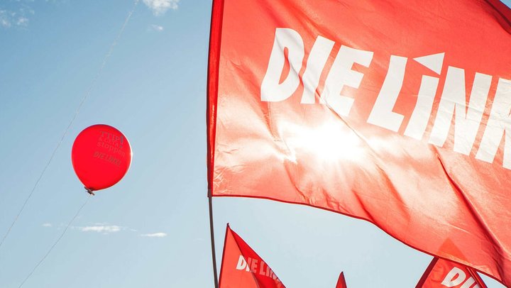 Fahne der Partei DIE LINKE vor einem roten Luftbalon, der vor blauem Himmel aufsteigt.