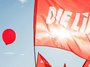 Fahne der Partei DIE LINKE vor einem roten Luftbalon, der vor blauem Himmel aufsteigt.